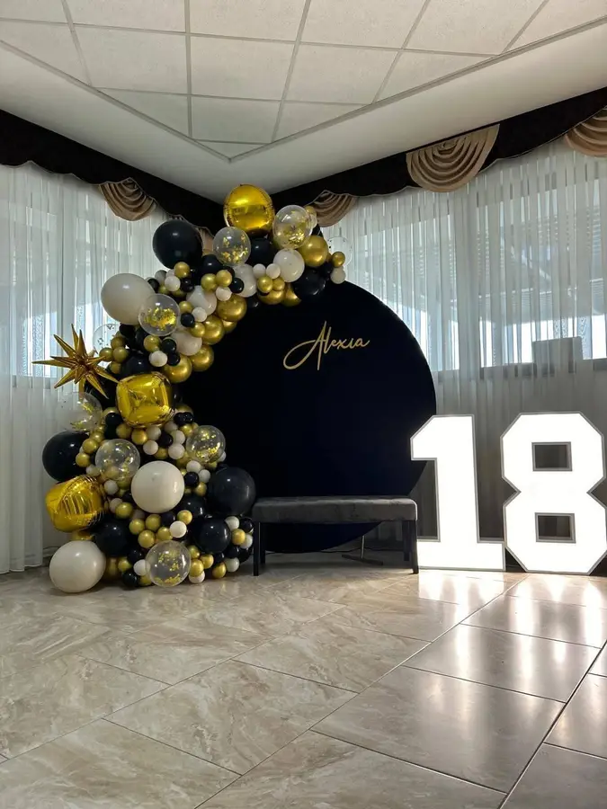 Arcadă de baloane negru, auriu și crem, cu numele Alexia scris cu auriu și cifra 18 luminoasă